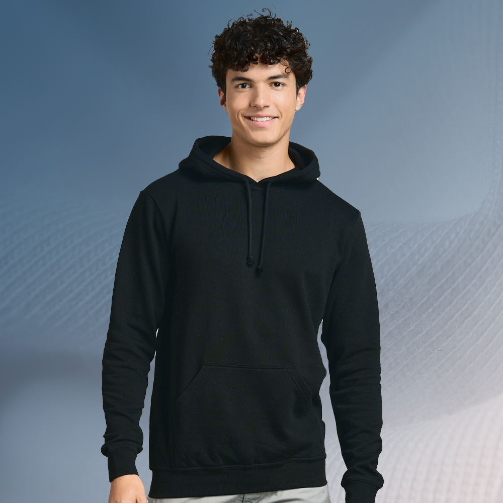 Ein junger Mann trägt einen schwarzen Hoody mit Kängurutasche und Kapuze, steht vor einem graublauen Hintergrund mit Stoffstruktur und lächelt leicht.