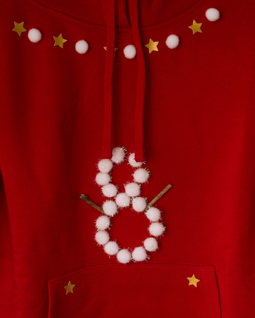 Nahaufnahme eines roten Hoodies, dekoriert mit weißen Pompons und goldenen Sternen.