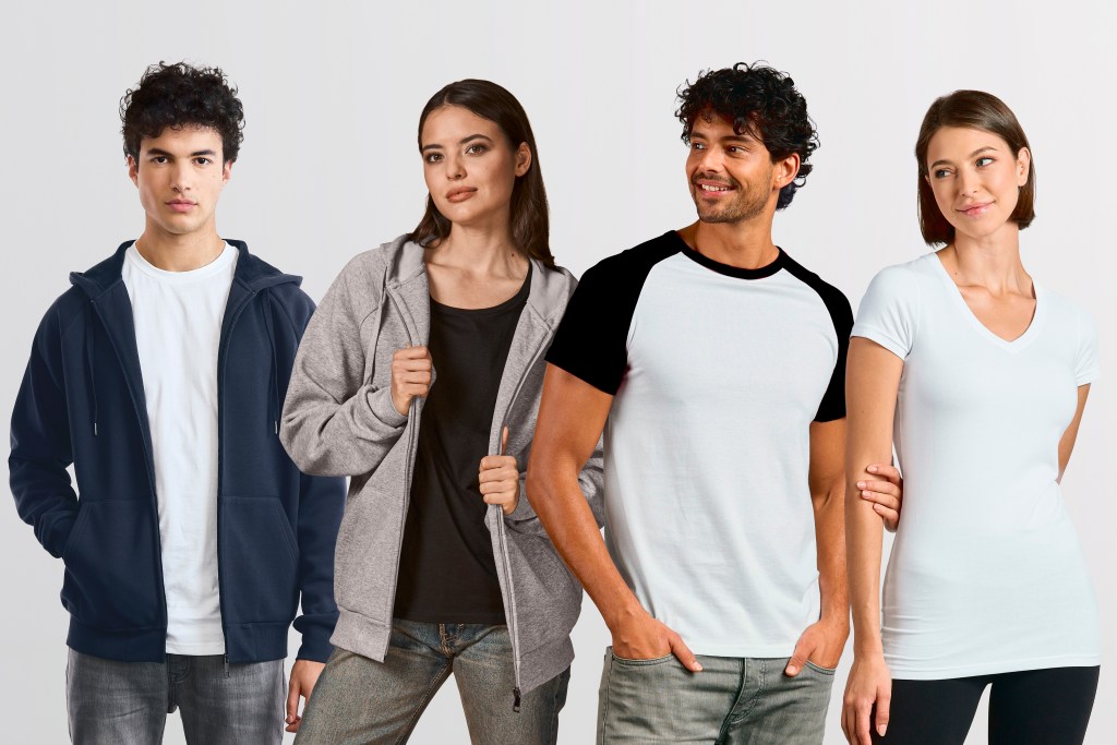Vier junge Erwachsene stehen nebeneinander vor hellem Hintergrund und tragen schlichte Freizeitkleidung wie T-Shirts, Hoodie und Jacke.
