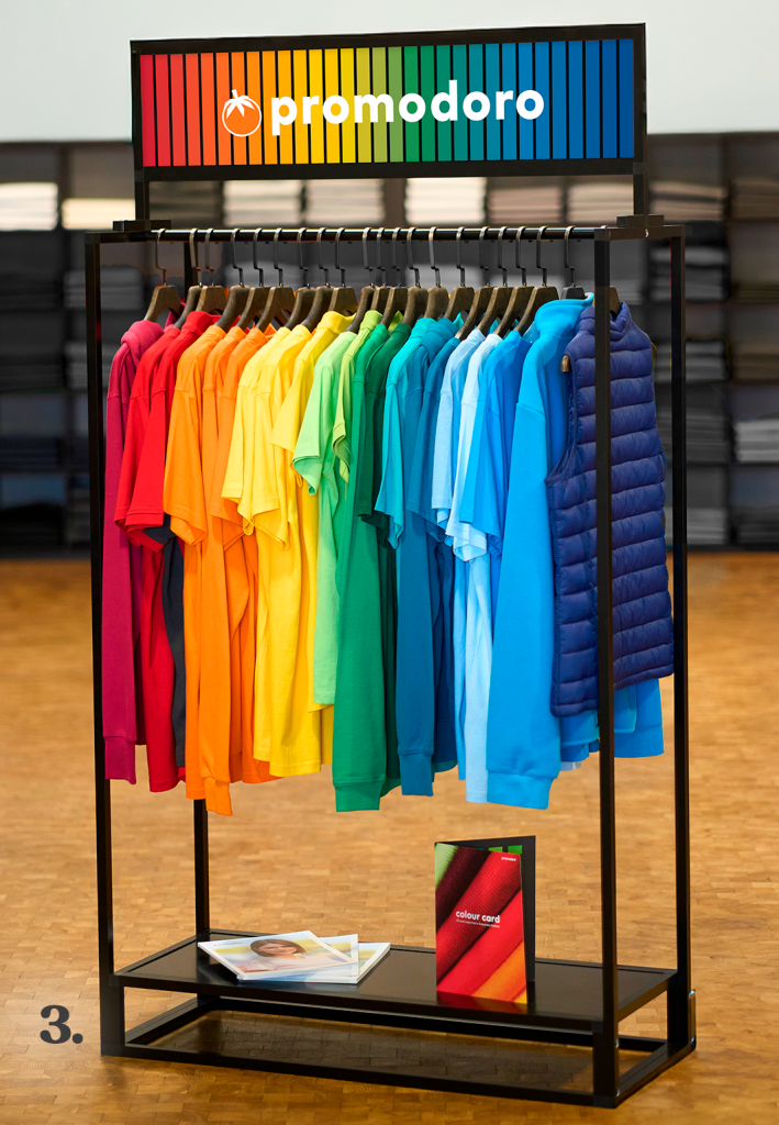 Kleiderständer mit promodoro-Logo und T-Shirts sowie Jacken in vielen Farben, übersichtlich nach Farbtönen sortiert.